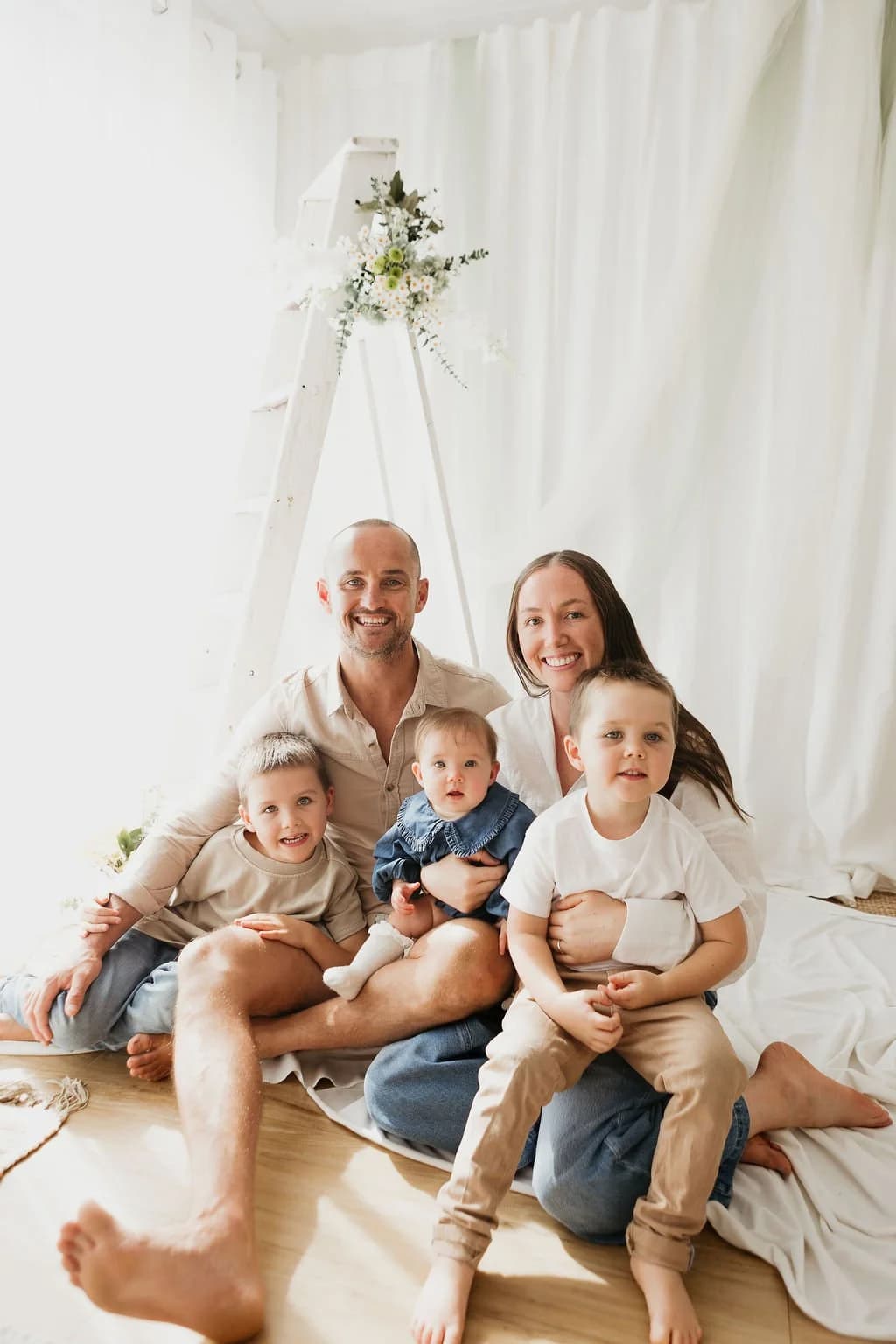 Tam, her husband Ant and their three young boys sitting together and smiling in a white studio.