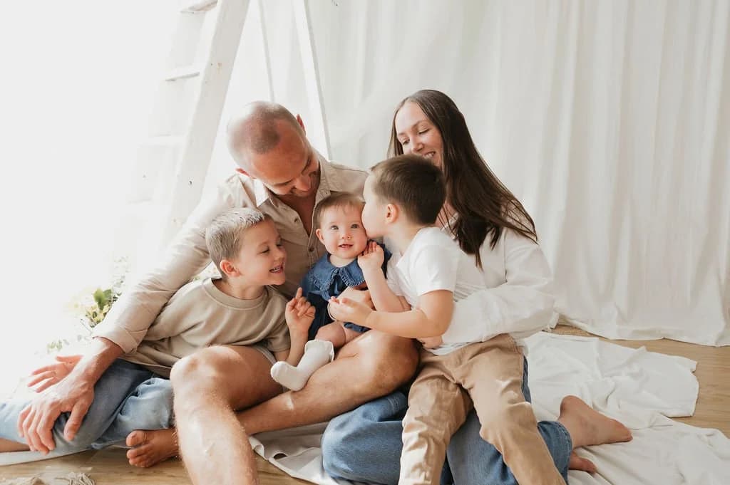 Tam and her husband Ant laughing with their three young boys, one of them kissing the baby’s cheek.