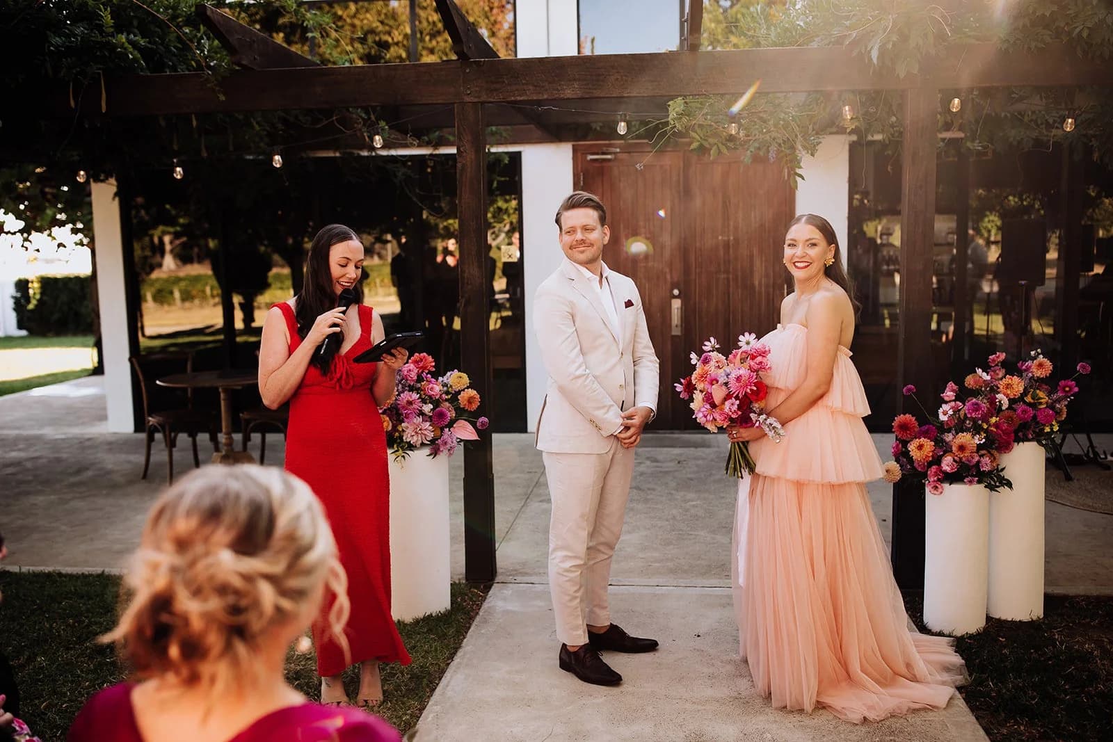Tam leading Maddy and Andrew’s ceremony beneath a flower-lined pergola.